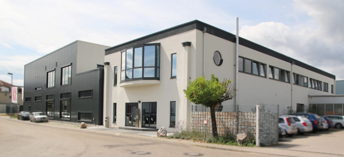 Modern commercial building with white and dark gray exterior, large windows, and multiple parked cars in front along a street.