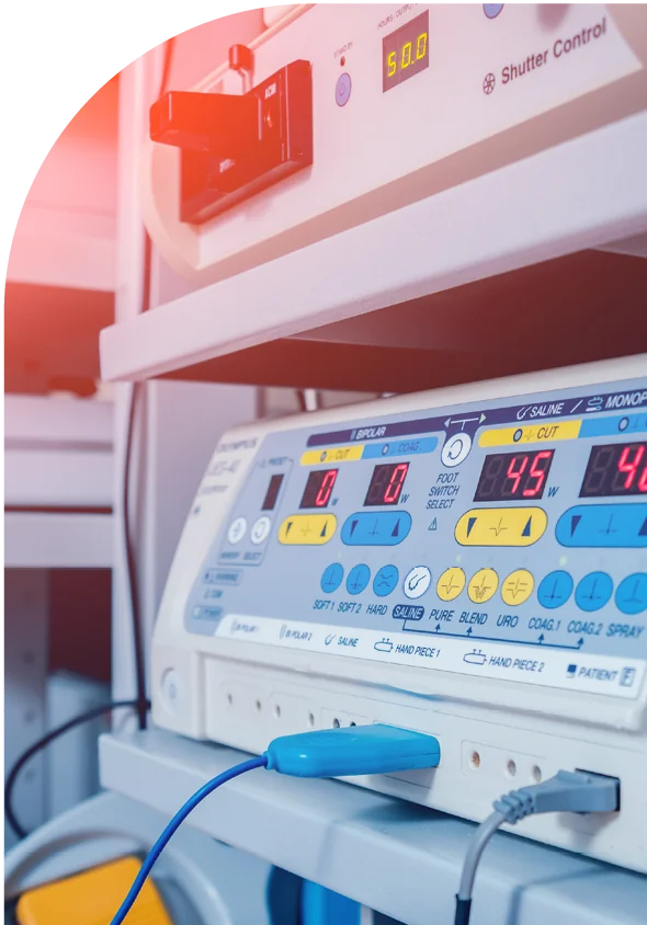 Close-up of medical equipment with digital displays, buttons, and a blue probe attached, set on a metal shelf in a clinical setting.